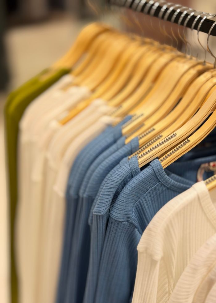 digital-01 A row of neatly arranged colorful clothes on wooden hangers in a retail store setting.