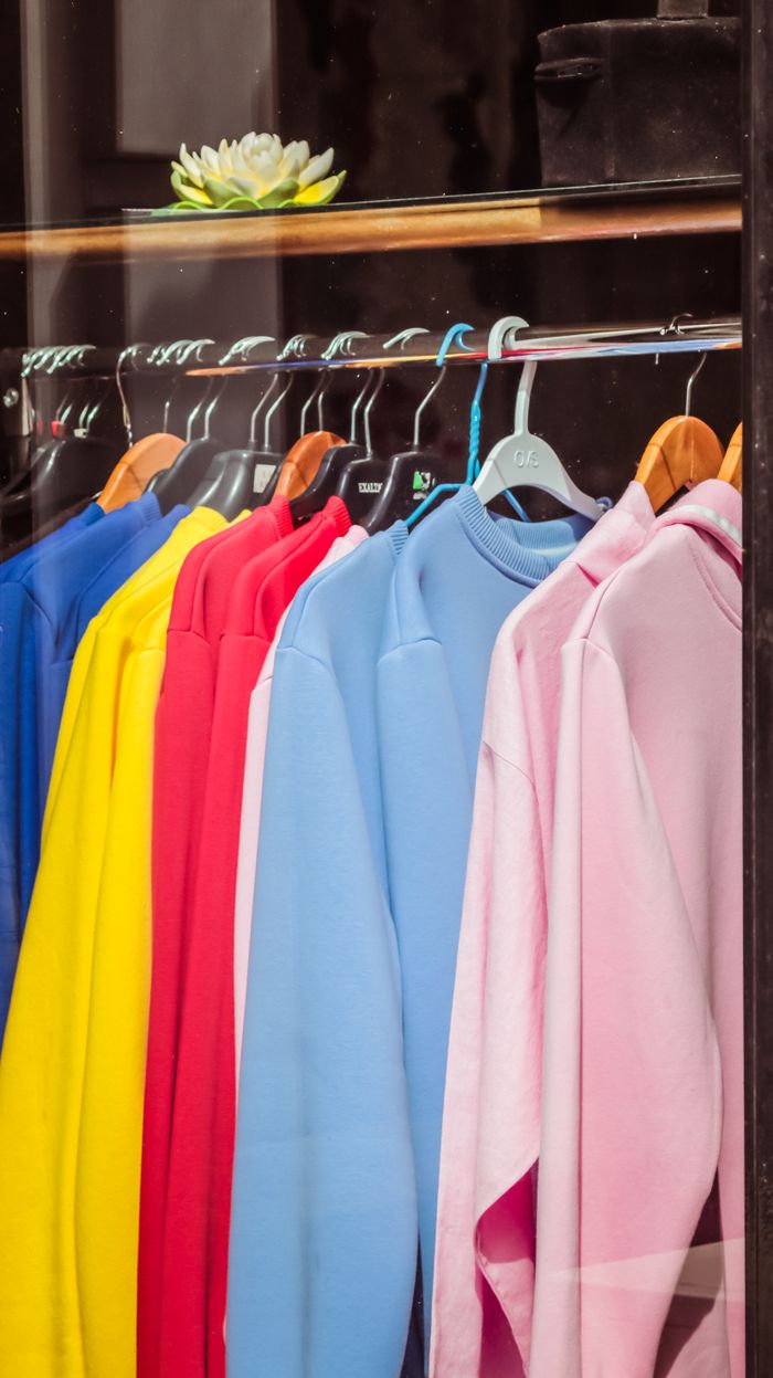 our-story Through glass collection of multicolored sweatshirts hanging on rack on showcase of modern fashion store